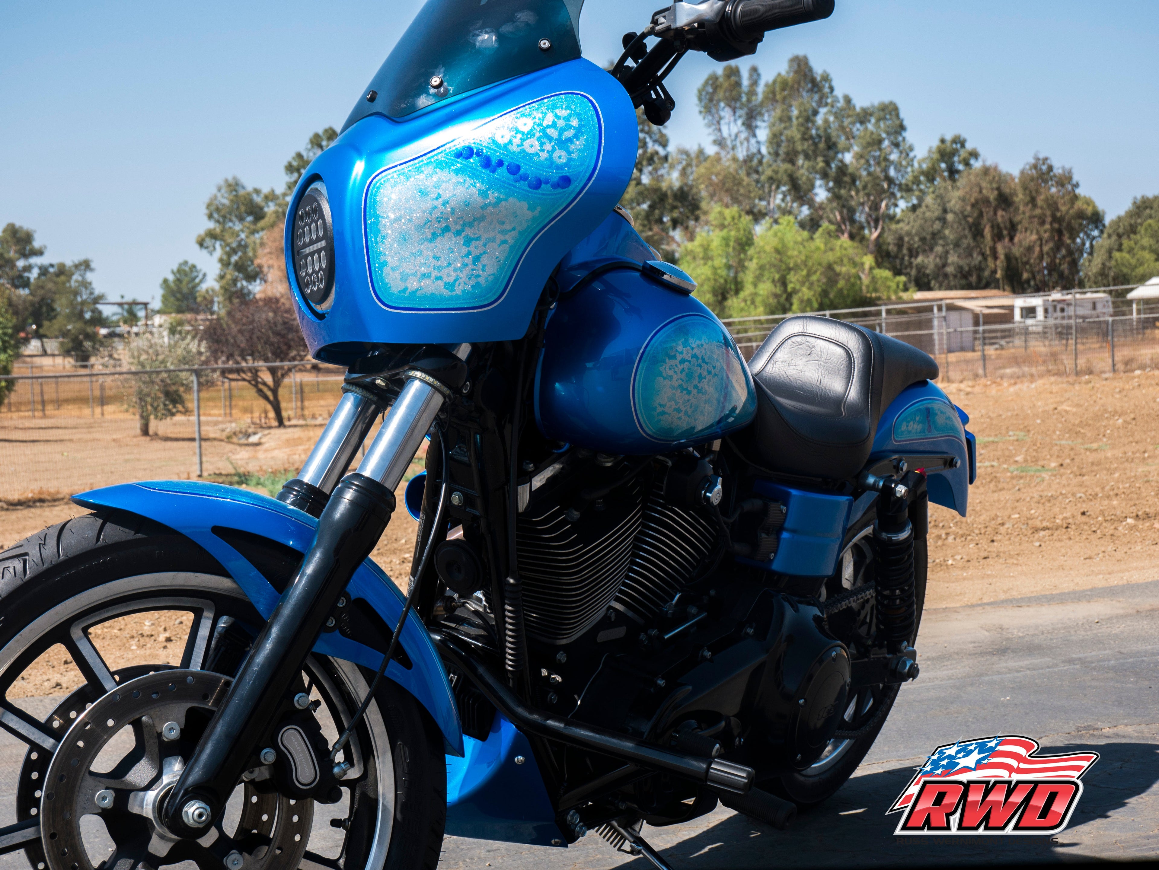 A custom blue RWD V-Twin motorcycle with a fairing, LED headlight, and custom paint details, parked outdoors.
