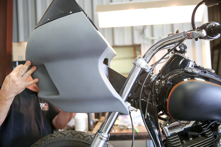 RWD V-Twin motorcycle with a grey primer fairing being fitted by a person's hands, showcasing the RWD V-Twin fairing, chrome handlebars, and black fuel tank with an orange stripe.
